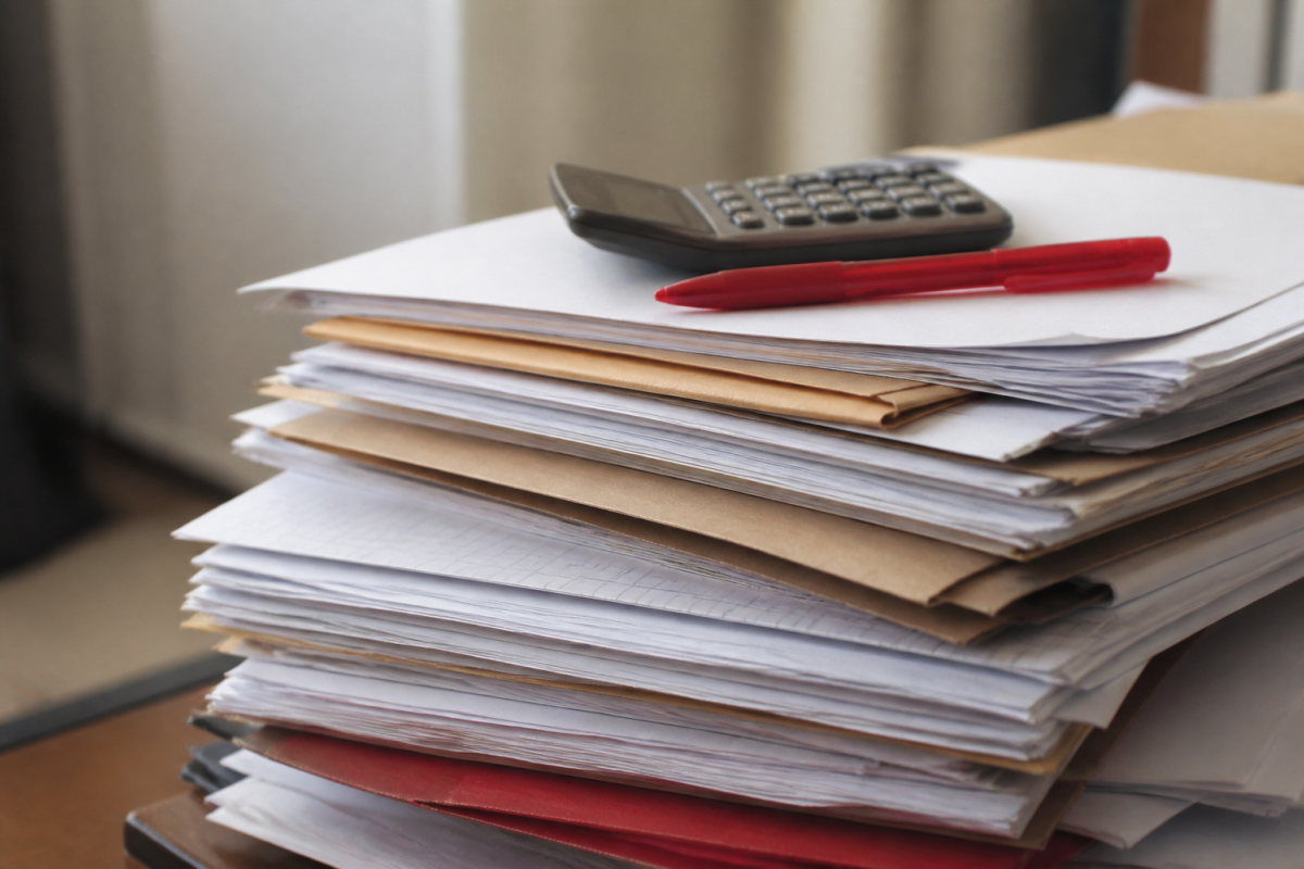 Pile de documents administratifs avec calculatrice et stylo rouge