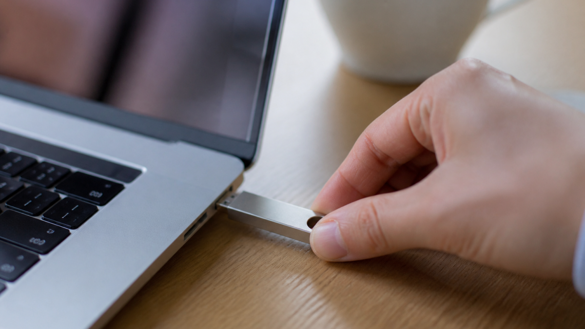 Main inserant cle USB argentee dans port lateral ordinateur Mac