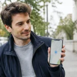 Homme debout tenant smartphone affichant carte point bleu