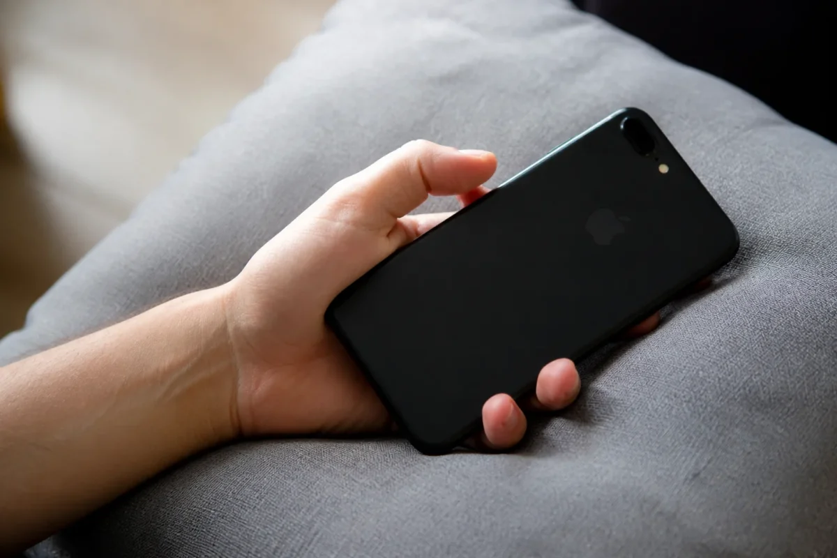 Main tenant un iPhone noir sur un coussin gris