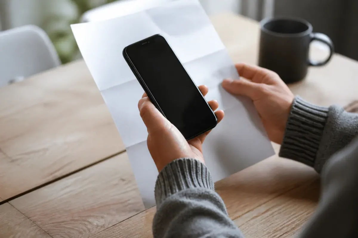 Mains tenant un smartphone noir devant une facture imprimee